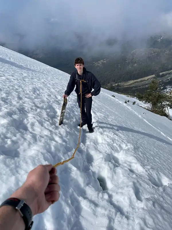 Holding a rope while a friend climbs the snow with a wheel-less skateboard